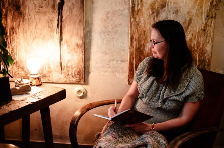 Brandový portrét básnířky držící v ruce knihu sedící na křesle u stolu s lampou
