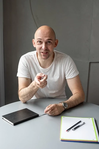 Realitní makléř Rosťa Očenášek sedí u stolu s dokumenty v rukách a počítačem na stole