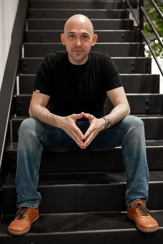 Profesionální portrét muže v černém tričku sedícího na schodech se sepjatýma rukama